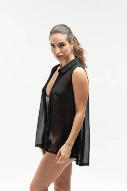 Stüdyoda çıplak poz veren genç ve güzel bir kız. Siyah bir gömlekle duruyor.