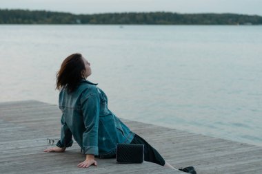 Genç ve güzel bir kadın gölün yanındaki tahta köprüde oturuyor.