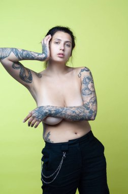 Stüdyoda çıplak poz veren dövmeli güzel bir kadın.