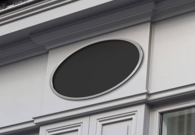 Gri bir dükkanın ön cephesinde siyah dairesel vitrin. Sokakta boş marka tabela çerçevesi