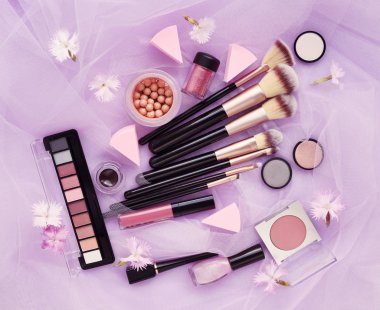 Çiçekli pembe peçe arka plan üzerinde Dekoratif kozmetik ve makyaj fırça. Üstten görünüm