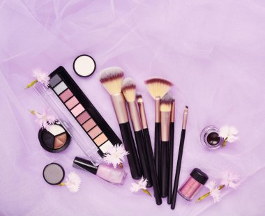 Çiçekli pembe peçe arka plan üzerinde Dekoratif kozmetik ve makyaj fırça. Üstten görünüm