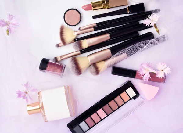 Çiçekli pembe peçe arka plan üzerinde Dekoratif kozmetik ve makyaj fırça. Üstten görünüm