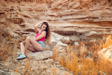 Öğleden sonra sıcak havalarda kayanın üzerinde oturan güzel genç kadın