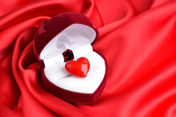 Open heart-shaped gift box with glass heart on red satin fabric background. Valentines Day background