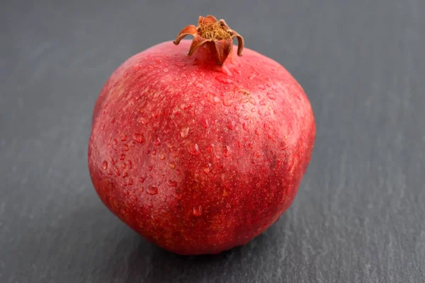 Granatäpple med droppar vatten på svart sten bakgrund — Stockfoto