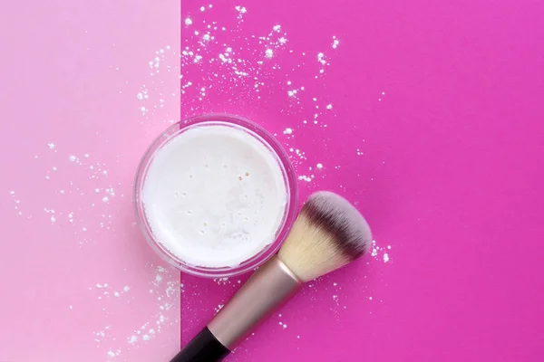 Mineral powder foundation and a brush on bright pink background.