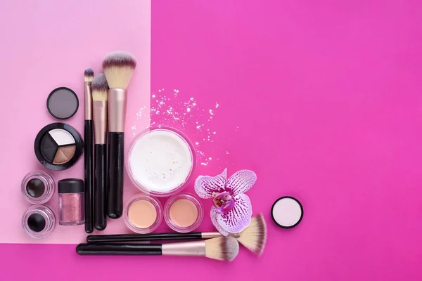 Cepillo de maquillaje y cosméticos decorativos y una flor de orquídea en rosa — Foto de Stock