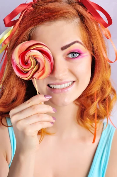 Jovem atraente menina de cabelo vermelho com maquiagem criativa com pirulito colorido — Fotografia de Stock