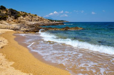 Plajı, kayaları ve şeffaf suyu olan güzel bir deniz manzarası.