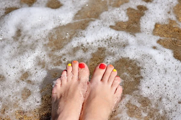 Nasse Frauenfüße am Strand in der Brandung des Meeres. Urlaub — Stockfoto