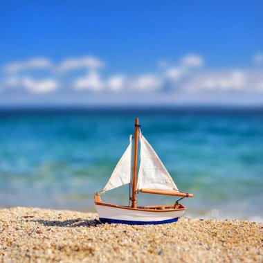 Deniz ve mavi gökyüzünün arka planına karşı sahilde minyatür oyuncak yelkenli. Tatil ve seyahat konsepti.