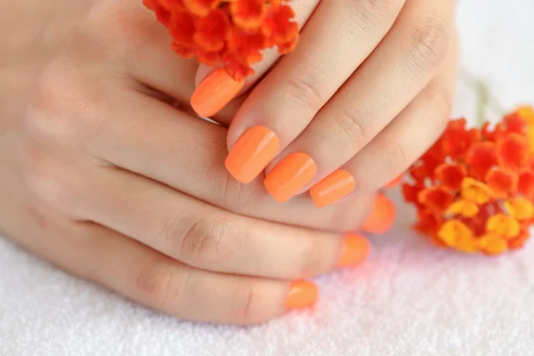 Mãos de uma mulher com manicure laranja em unhas e flores vermelho-alaranjadas — Fotografia de Stock