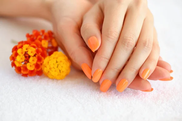 Manos de una mujer con manicura naranja en las uñas y flores rojo-anaranjadas — Foto de Stock