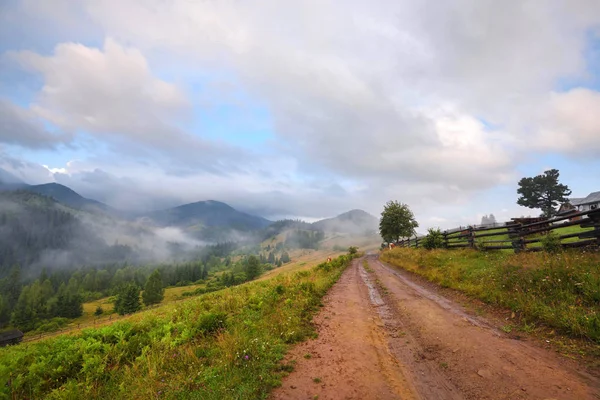 Paisagem de montanha incrível com nevoeiro e com uma estrada de terra . — Fotografia de Stock