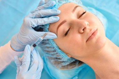 Kozmetik uzmanı güzellik salonunda güzel bir kadının yüzüne iğne yapıyor. Kozmetoloji kavramı.