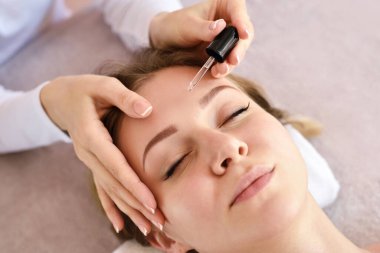 Kozmetik uzmanı kozmetik merkezinde kızın yüzüne kozmetik serumu uyguluyor. Spa prosedürleri.