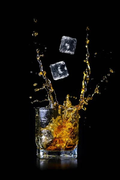 Szklanka Rozpryskującej Się Whisky Lub Innego Alkoholu Kostką Lodu Czarnym — Zdjęcie stockowe