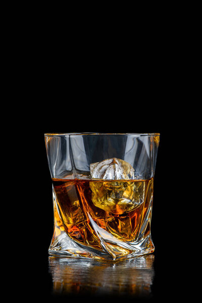 Glass of whiskey or other alcohol with cube ice on black background