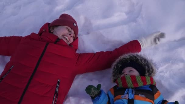 Gelukkig moeder en klein kind spelen in de sneeuw, maken een engel van de sneeuw. Happy familie, zonnige winterdag, slowmotion — Stockvideo