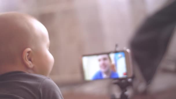 Маленький хлопчик дивиться на свого батька на відеочаті і торкається екрана смартфона. 4K вид ззаду крупним планом кадри — стокове відео