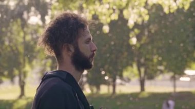 Portre bir profil sunshining içinde ayakta park yaz bir genç sakallı adam. 4 k yan görünümü slowmo
