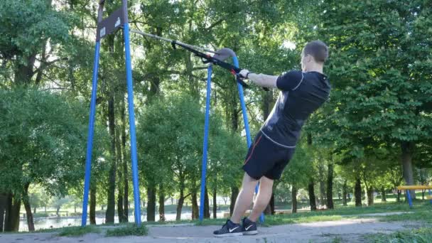 Man börjar göra pull-up exercerande på gym loopar i sommaren park. 4 k slow motion film — Stockvideo