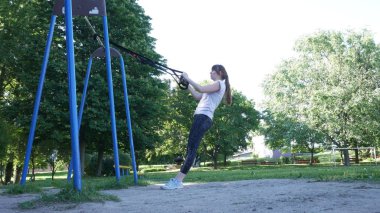 Genç kadının yoğun pull-up fitness üzerinde egzersiz yapması yaz parkta döngüler. 4 k ağır çekim görüntüleri