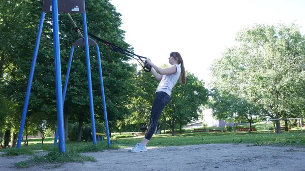 Młoda kobieta robi, wykonując intensywne pull-up na fitness pętle w lato park. 4 k zwolnionym tempie nagrania — Zdjęcie stockowe