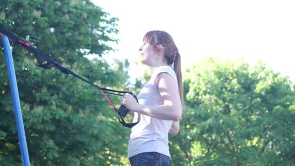 公園内のフィットネス trx ストラップにプルアップを行う若い女性。4 k が遅い mo クローズ アップ映像 — ストック動画