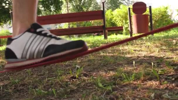 Close-up shot of mans foot in sneakers walkining on the slackline and then jumps down from it. 4K slow mo footage — Stock Video