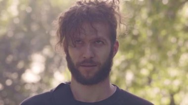 karizmatik kamera seyir, gülümseyen adam sakallı ve alnına saç sunshining Park'ta esiyor. 4 k ön görünüm slowmo