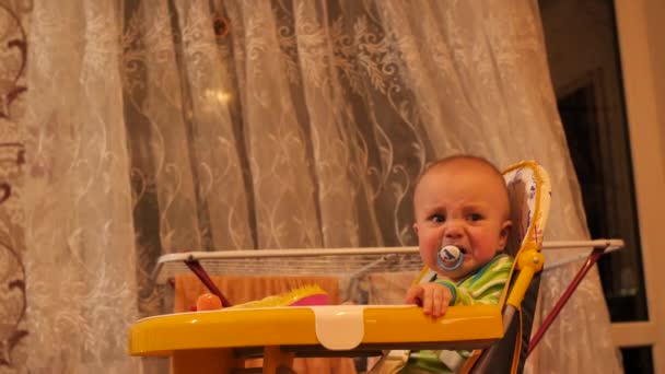 Pequeño niño con chupete en la boca que se sienta en silla y llora 4K lento mo — Vídeos de Stock