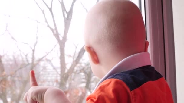Het kind verheugt zich lachend. Met deze methode tekent een hand in het venster. Slow-Motion. Happy baby kijkt uit het raam. — Stockvideo