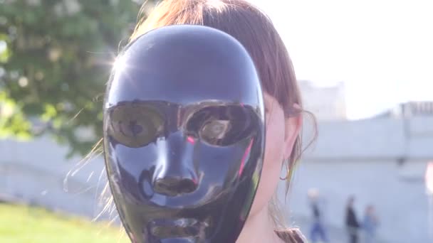 Portrait d'une jeune jolie femme charismatique qui cache son visage derrière le masque noir puis le met de côté et sourit sur le fond de la ville, gros plan vidéo au ralenti en 4K — Video