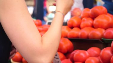 Çarşıda domatesleri seçen genç ve güzel bir kadın. Arka planda tanınmayan bir satıcı var. Yavaş çekim videosu 4K 'de.