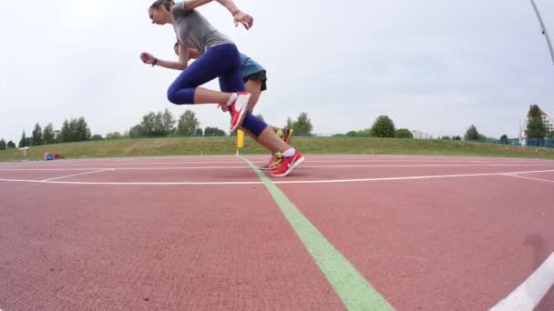 Dos jóvenes deportistas hombre y mujer comienzan a correr en pista de atletismo durante un día de entrenamiento en cámara 4K en cámara UHD — Vídeos de Stock