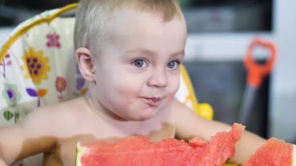 Mooie kleine jongen het eten van een watermeloen aan de kinderen tafel en schudden zijn hoofd gelukkig glimlachen close-up te bekijken slow mo video in 4k — Stockvideo