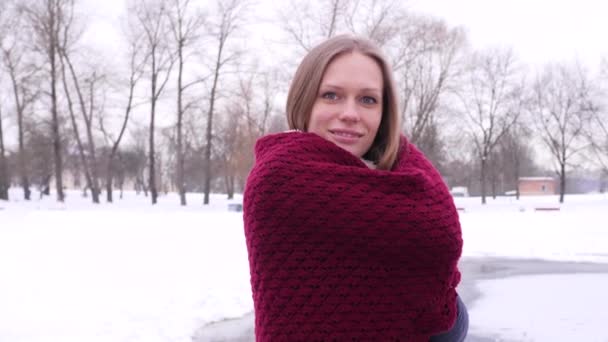 Portrét modré oči s usměvavou ženou, která si na ramena klade šály a dívá se do kamery v zimním městském parku v 4k pomalý pohyb zblízka video. — Stock video