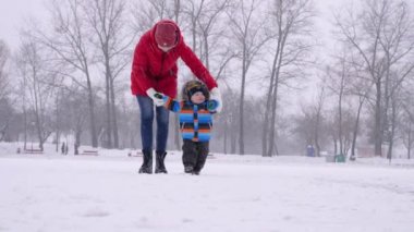 Güzel bir bebeği olan mutlu genç anne, karlı bir havada bir kış parkında yürüyor.