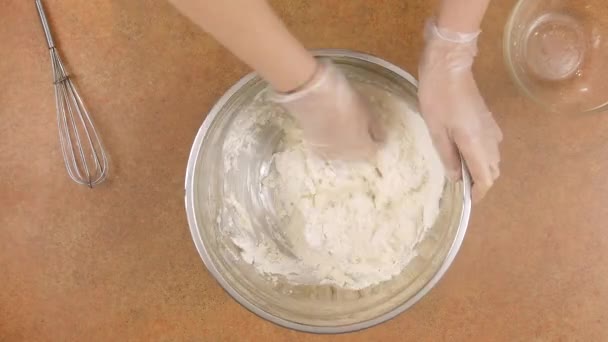 Pour water into a bowl of flour and knead the dough with your hands.A man or a woman knead the dough with their hands in gloves. — Stock Video