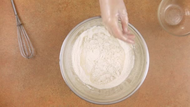 Un homme ou une femme pétrissent la pâte avec leurs mains dans des gants. Versez de l'eau dans un bol de farine et pétrissez la pâte avec vos mains . — Video