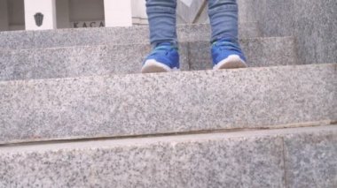 Mavi spor ayakkabıları ve kot elbise güneşli bahar günü arka planda şehir parkında adım granit merdiven adım aşağı gidiyor bir bebek çocuk ayaklar yakın. Eli küçük oğlunu tutan adam yardımcı olur