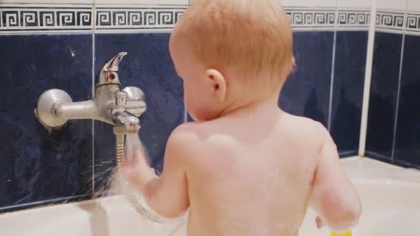 Kleiner Junge lacht und spielt mit Wasserstrahl in der Badewanne, die Hände seiner Mutter neben ihm in Zeitlupe Medium gedreht 4k Filmmaterial — Stockvideo
