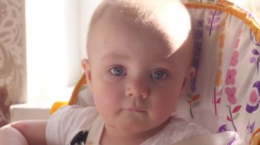 Güzel küçük oğlan çocuk masasında oturuyor, düşünceli bir şekilde kameraya bakıyor ve arka planda güneş ışığı penceresi ile etrafını çeviriyor.