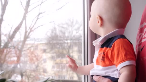 Primer plano de un niño pequeño que jugando junto a la ventana con su abuelo anciano en el fondo de un árbol detrás de la ventana en cámara lenta 4K video de interior — Vídeo de stock