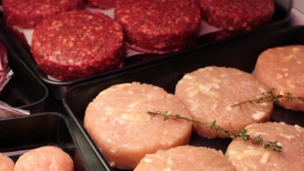 Rundvlees en kip schnitzels, gemarineerde stukjes ossenhaas verse rauw rundvlees met rozemarijn, plakjes spek liggen in zwarte trays op de winkel plank op vlees sectie klaar voor verkoop in slow mo camera — Stockvideo