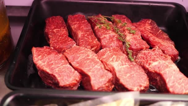 Stukjes ossenhaas vers rauw rundvlees met rozemarijn, varkensvlees en plakjes spek liggen in zwarte trays op de winkel plank klaar voor verkoop in slow mo camera Motion 4k video zonder mensen — Stockvideo