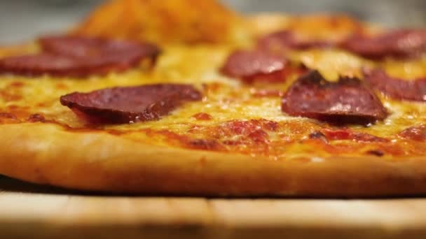 Fraîchement fait chaud appétissante pizza peperoni pose sur une table en bois par une figure floue de chef homme ou femme sur fond au ralenti vue rapprochée 4K vidéo — Video