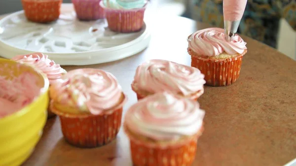 Decoración de la taza de pastel con crema. Usando la bolsa de cocina, confitero haciendo cupcakes multicolores para la fiesta. Shot de manos de las mujeres poniendo crema de mantequilla en los sabrosos pasteles, concepto de panadería casera —  Fotos de Stock